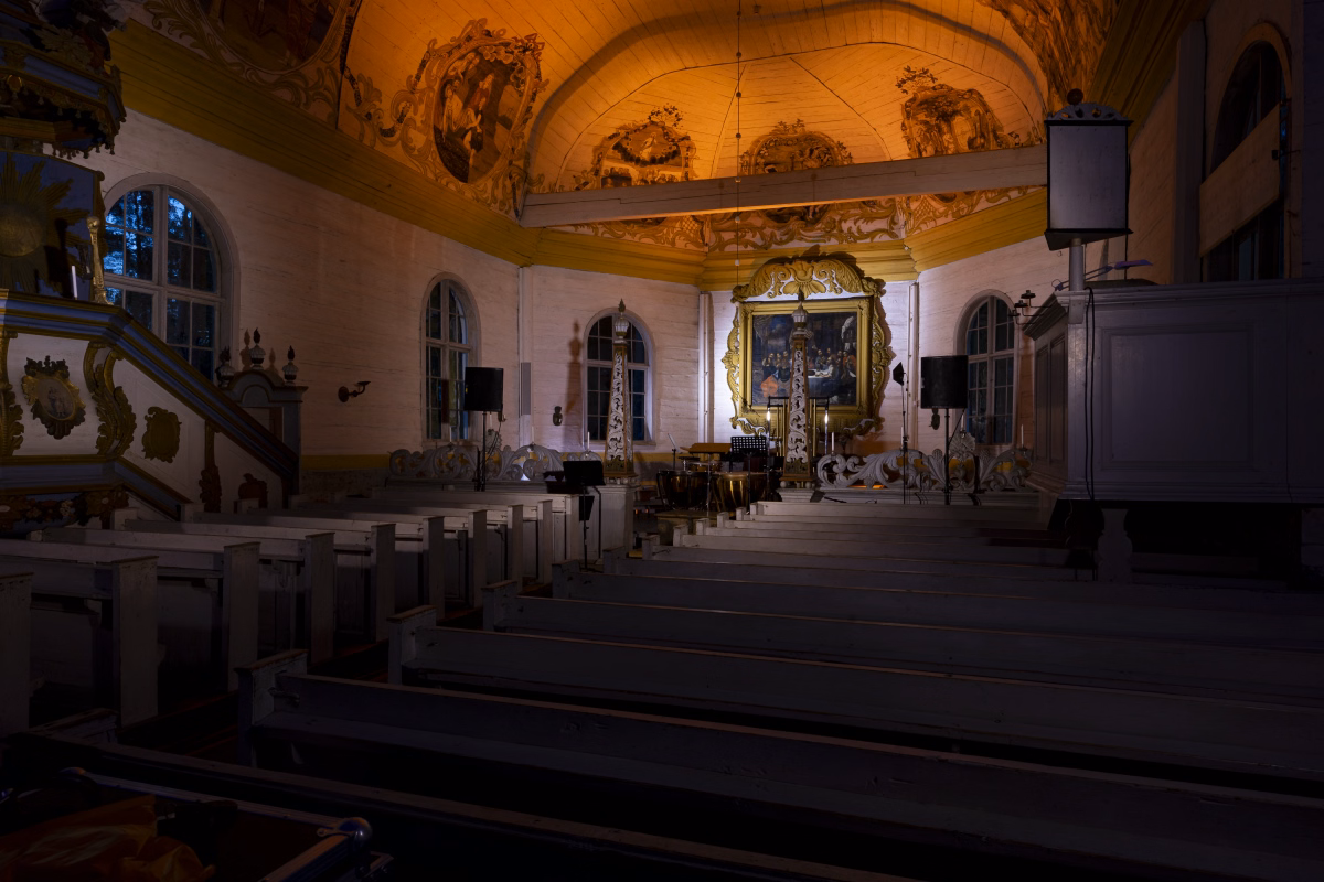 The altar end of the church seen across the empty pews before the audience arrived, ceiling frescoes lit warm and the percussion kit already in place.
