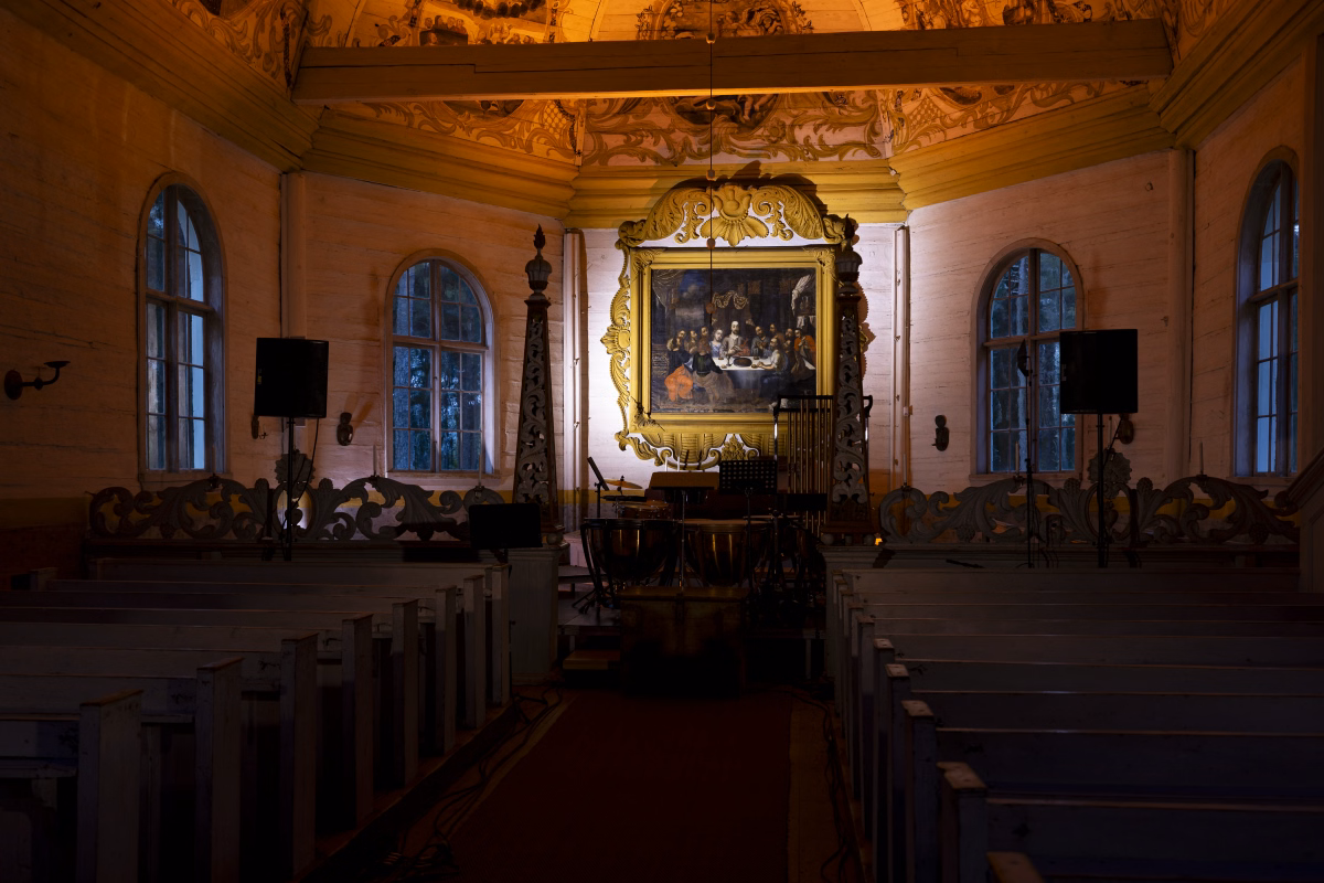 The altar end of the church lit warmly for the cantata, with the altarpiece painting, carved candle stands, PA speakers, and percussion set up in front of the pews.