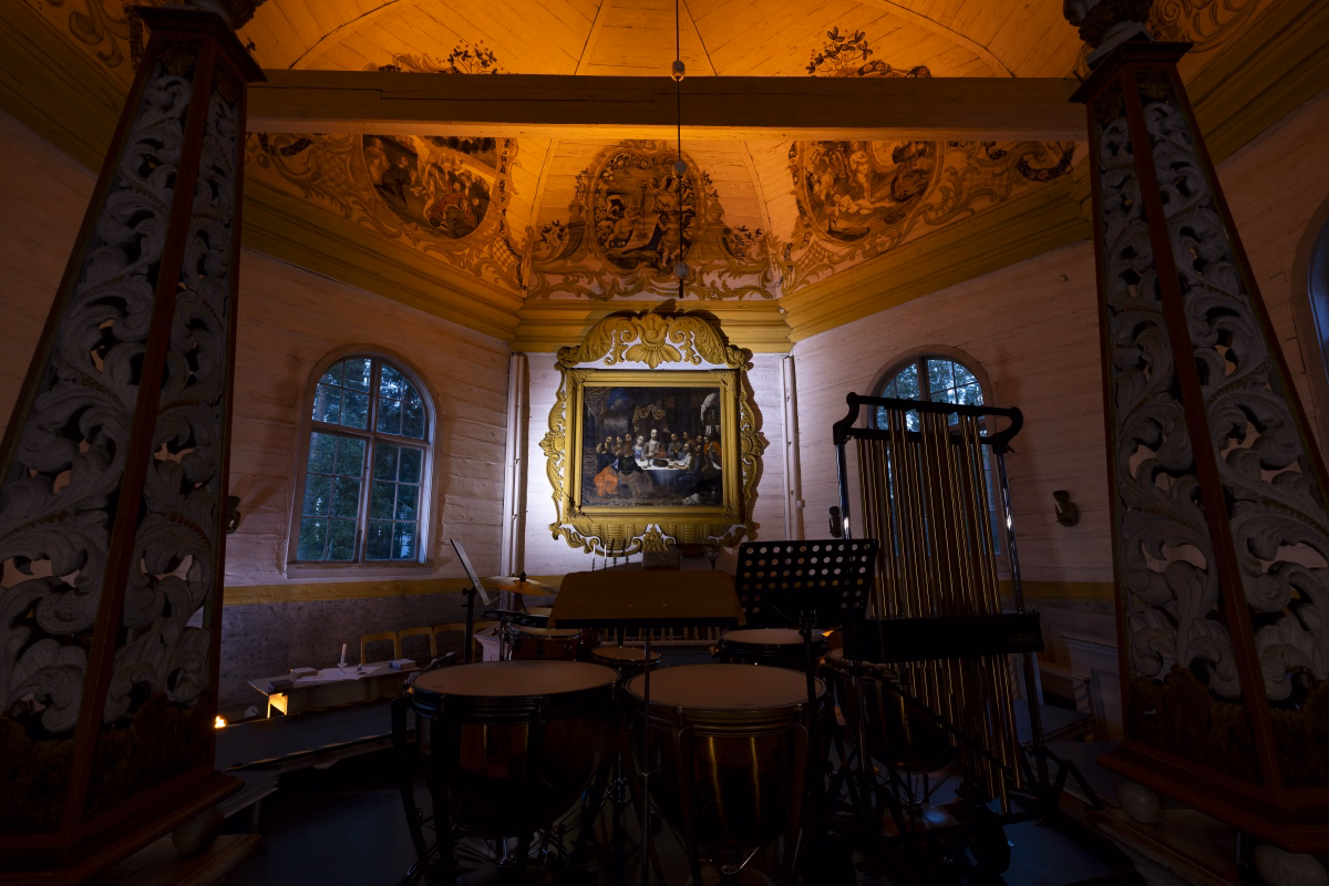 A closer view of the percussion setup at the altar, framed by the church&rsquo;s carved candle stands: timpani, tubular bells, and a music stand beneath the gilded altarpiece.