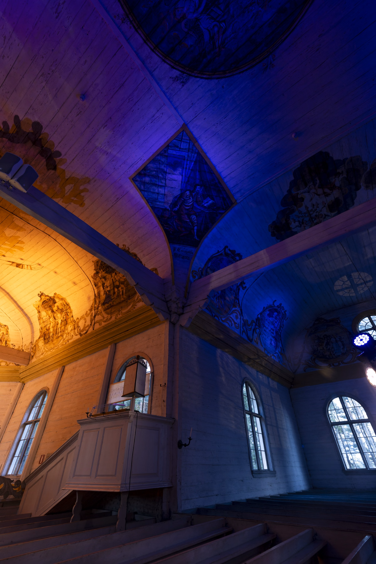 A close-up of the vaulted ceiling frescoes split between warm and blue light, with the pulpit visible in the corner.