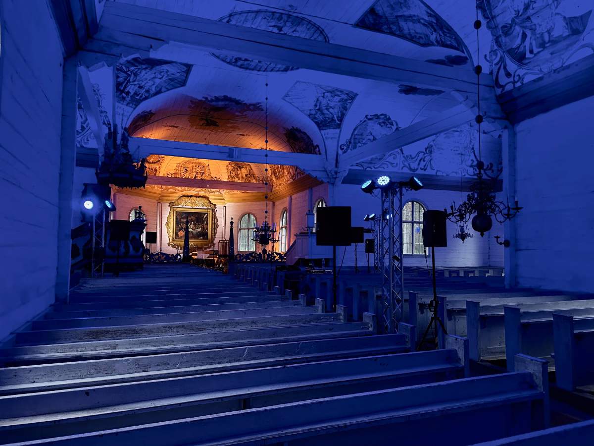 A wide-angle view of the nave in blue wash, with lighting trusses and fixtures visible on both sides and the altarpiece glowing warm in the distance.